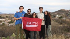 Five young adults stand outdoors on a hill holding a red flag that reads "FAITH THAT DOES JUSTICE.