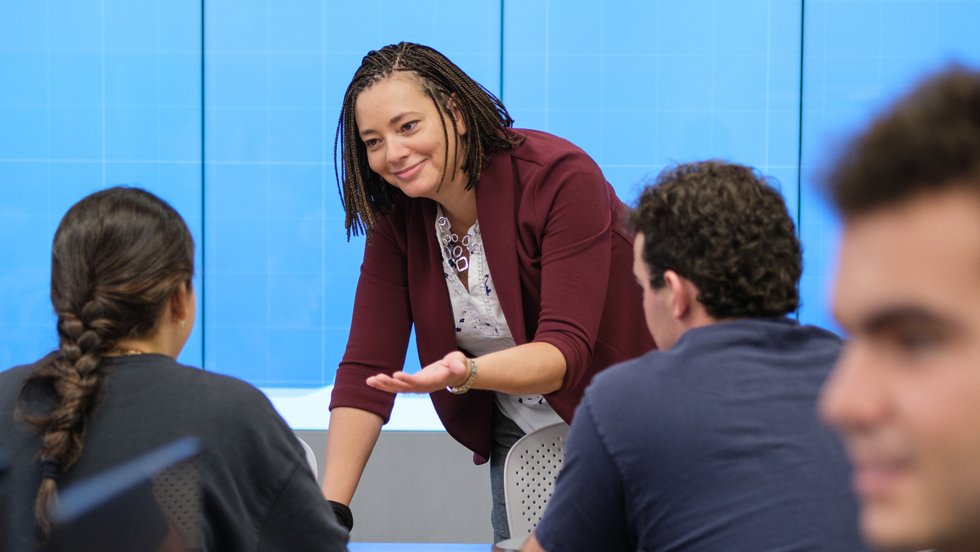 A faculty member speaking with students around a table.