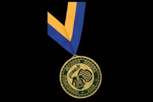 A circular gold medal, an alumni award for distinguished service, hangs from a blue and gold striped ribbon.