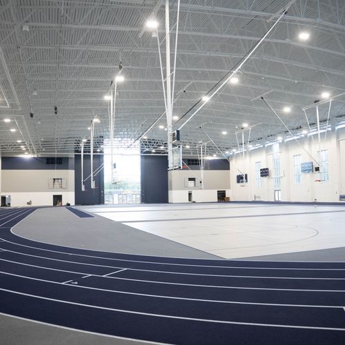 A large, indoor sports complex with a running track encircling a basketball court is brightly lit.