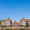 A large brick university building with multiple windows stands behind a sign reading John Carroll University under a clear.