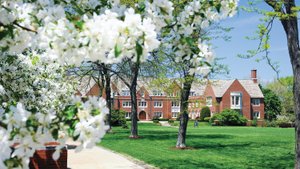 View of a red brick campus building at John Carroll University framed by blooming white flowers and green trees on a sunny.