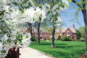 View of a red brick campus building at John Carroll University framed by blooming white flowers and green trees on a sunny.