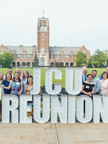 JCU alumni from the class of two thousand gather for their reunion on campus, posing with a large "JCU REUNION" sign and