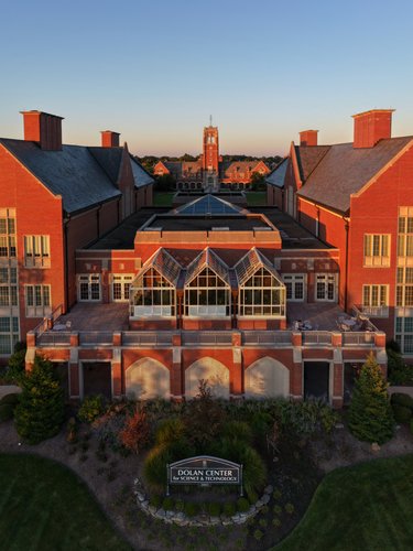 The grand red brick Dolan Center glows golden in the setting sun, with a wide lawn and patio for students to enjoy.