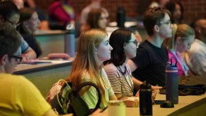 Students sit attentively in a lecture hall at John Carroll University with notebooks and water bottles on the desks.