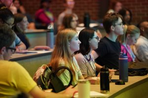 Students sit attentively in a lecture hall at John Carroll University with notebooks and water bottles on the desks.