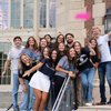 A group of smiling students wearing John Carroll University shirts celebrate with colorful confetti on campus steps.