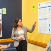 A woman in a gray blazer explains a research poster titled Effects of high-sodium chloride diet on anxious behavior to three.