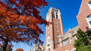A tall brick tower stands near a large tree with vibrant red leaves on the JCU campus; blue sky.