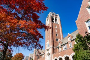 A tall brick tower stands near a large tree with vibrant red leaves on the JCU campus; blue sky.