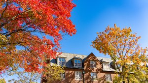 A brick campus building at John Carroll University is framed by trees with bright red and yellow autumn leaves under a clear.