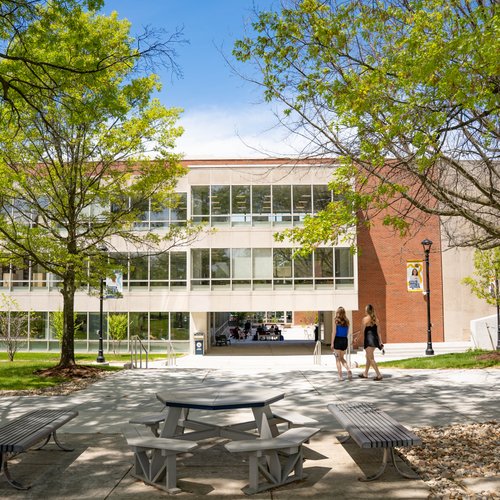 View of a campus building at John Carroll University framed by leafy trees with two people walking on the pathway.