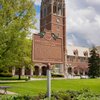 A historical marker for John Carroll University stands in front of a tall brick clock tower and a campus building framed by.