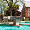 View of a Class of 1964 fountain with water flowing into a pool, framed by leafy trees and campus buildings.