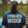 Person with long dark hair tied in a ponytail wearing a navy shirt that reads living the mission.