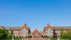 View of a large red brick campus building at John Carroll University framed by green trees and a clear blue sky.