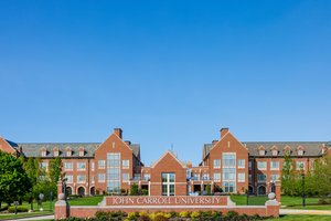 View of a large red brick campus building at John Carroll University framed by green trees and a clear blue sky.