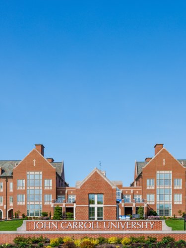 View of a large red brick campus building at John Carroll University framed by green trees and a clear blue sky.
