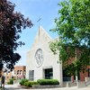 View of Saint Francis Chapel at John Carroll University framed by green and dark red trees under a clear blue sky.