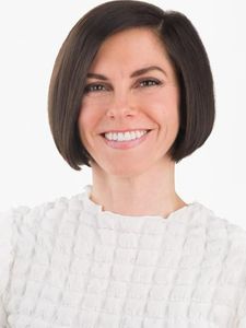 A woman with straight dark hair in a bob cut smiles while wearing a textured white top against a white background.