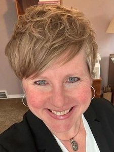 A JCU faculty member with short blonde hair and blue eyes smiles warmly, presenting herself in a black blazer and silver