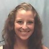 A woman with long wavy brown hair smiles at the camera against a plain light blue background.