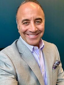 A smiling JCU faculty member with light green eyes, wearing a grey blazer and purple shirt