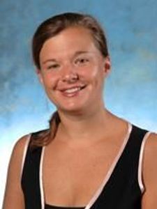A smiling woman with brown hair pulled back wearing a black sleeveless top against a blue background.