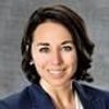A JCU faculty member smiles warmly, wearing a dark blazer. Her short, dark hair frames her face against a gray background.