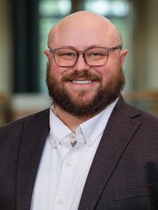 A JCU faculty member, a man with a bald head, beard, and glasses, offers a warm, broad smile for his portrait.