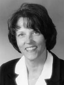 A black and white portrait of a woman with short dark hair smiling and wearing a dark blazer over a light blouse.