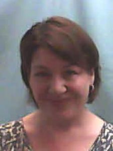 A person with short brown hair and light skin is smiling slightly against a plain light blue background.