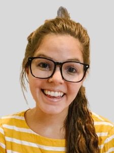 A smiling woman with long brown hair tied back and wearing large black glasses and a yellow and white striped shirt.