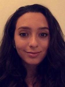 A JCU faculty member with dark, wavy hair and a gentle smile looks directly at the viewer for her professional portrait.