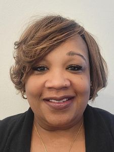 A woman with short light brown hair smiles at the camera against a plain light background.