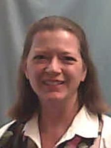 A woman with shoulder-length brown hair smiles slightly against a plain gray background.