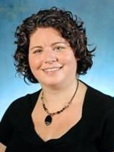 A woman with curly dark hair smiles at the camera against a blue gradient background.