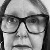 Close-up black and white photo of an older woman wearing large rectangular glasses and hoop earrings looking slightly upward.