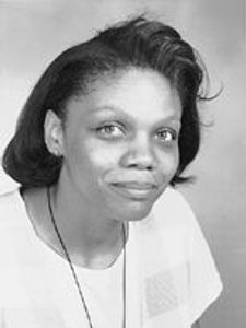 A black and white portrait of a woman with short hair wearing a light-colored top, looking slightly to the side with a calm.