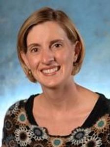 A woman with short light brown hair smiles at the camera against a blue-gray mottled background.