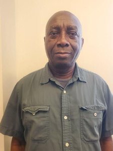 A JCU faculty member, a bald man with dark skin, smiles gently for his portrait, wearing a dark green shirt.