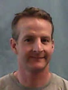 A man with short brown hair and a slight smile is shown against a plain gray background.