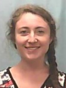 A woman with light skin and brown hair styled in a braid smiles at the camera against a plain gray background.