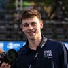 A young man wearing a navy blue polo shirt with Tennis in the Land logo smiles while holding a camera.