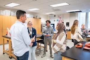 A man talks to three smiling students standing in a science classroom with anatomical models on tables.
