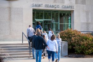 A group of people walk up steps toward the glass entrance of a building labeled Saint Francis Chapel.