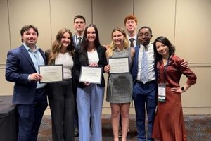 Nine students pose together, holding certificates; they smile for the camera, celebrating an event.