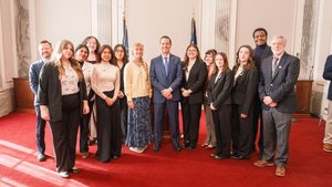 Students and a man in a suit stand together in a formal room, smiling for a photograph.