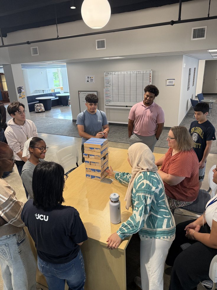 Bridge students and staff gathered around a table during a stacking-block game.